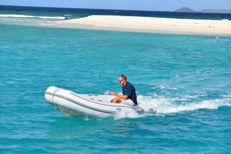 Un hombre conduce un yate de velocidad a través del agua azul con un banco de arena blanca en el fondo
